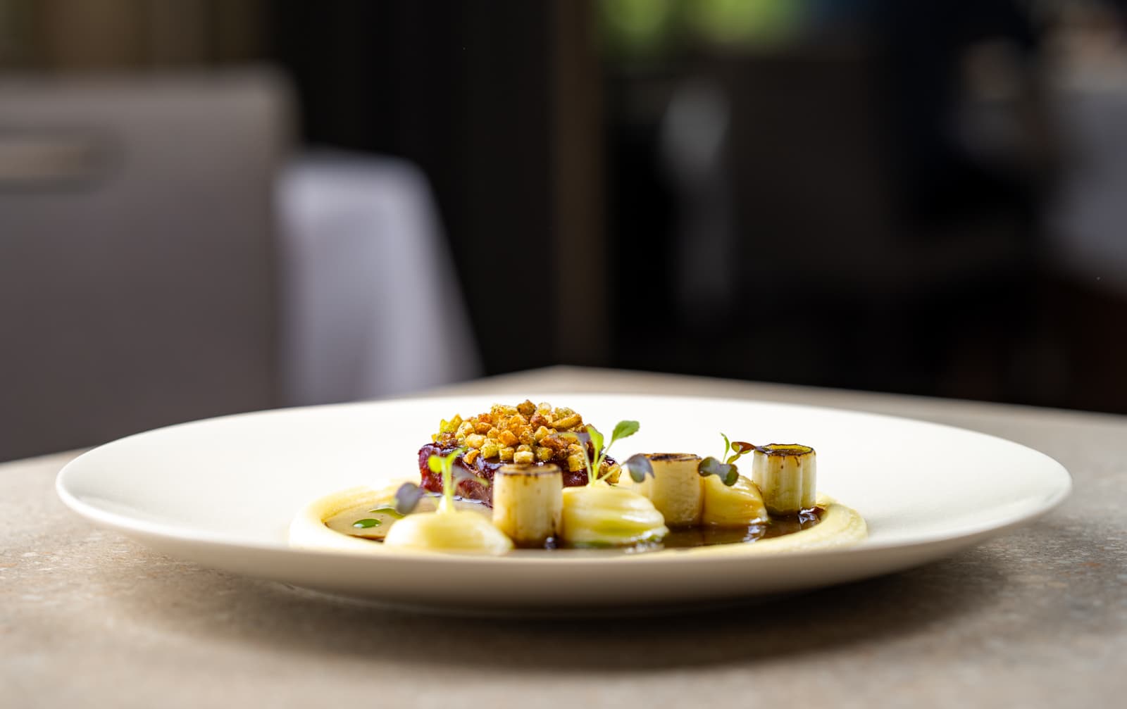 Een verfijnd opgemaakt gerecht met gouden accenten, groenten en saus, in zacht licht bij Landgoed Groenendaal.